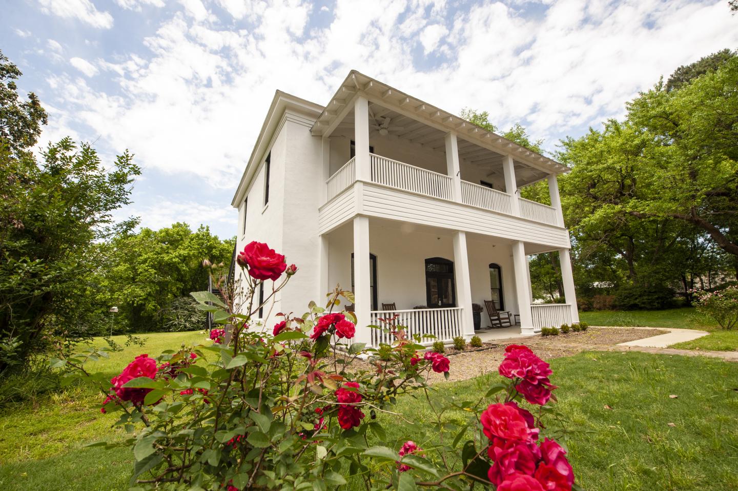 White house with two stories, surrounded by green lawn and red roses.