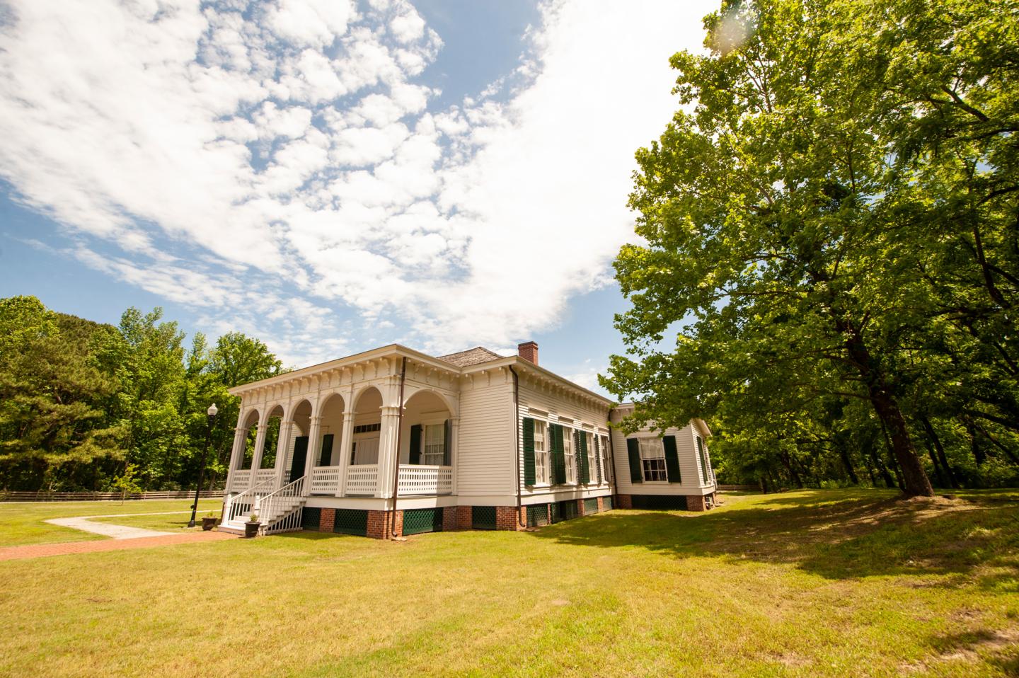 Historic white house with arched porch, surrounded by trees under a partly cloudy sky.
