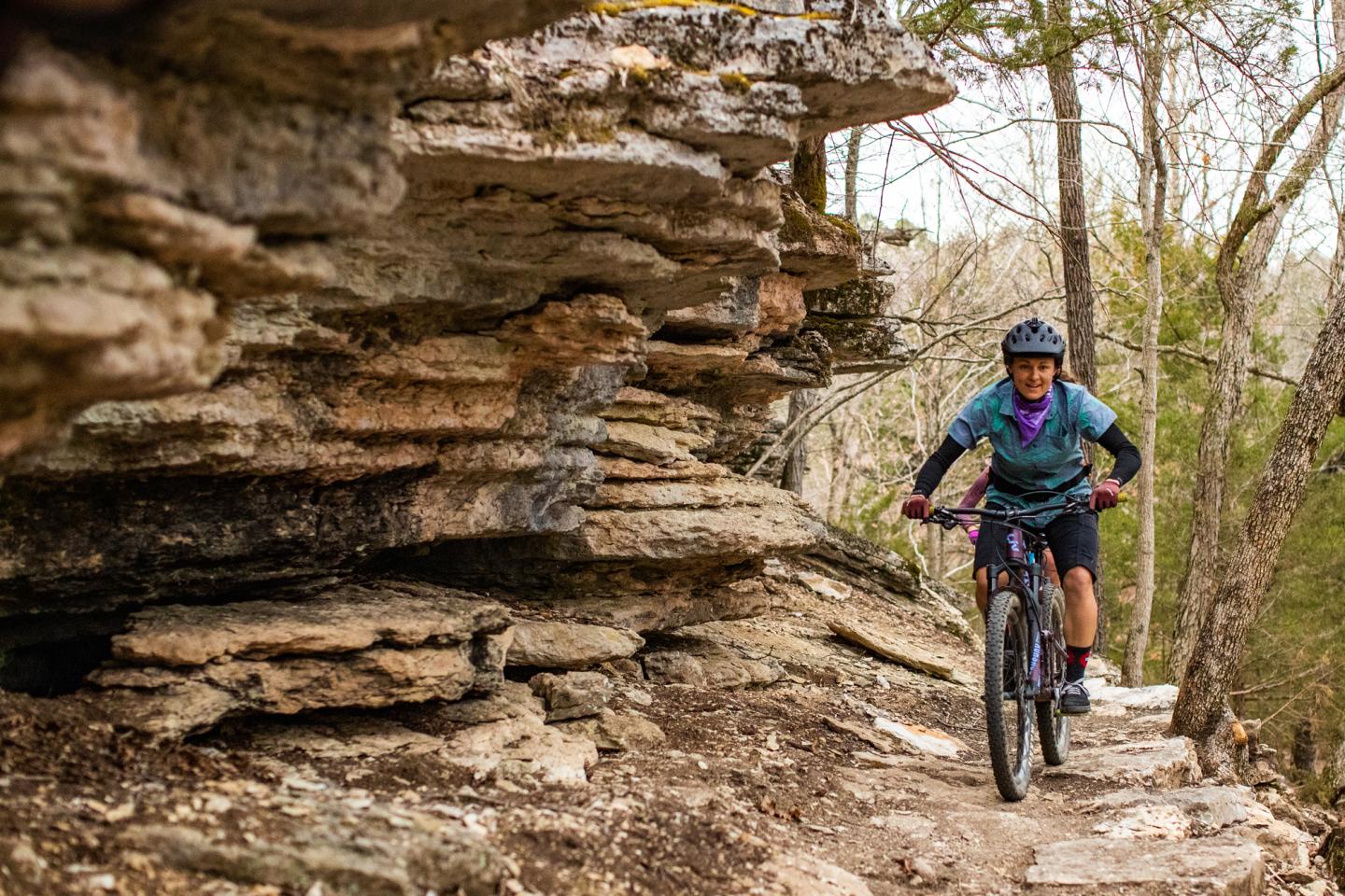 Mountain biker riding on rocky trail through forest.