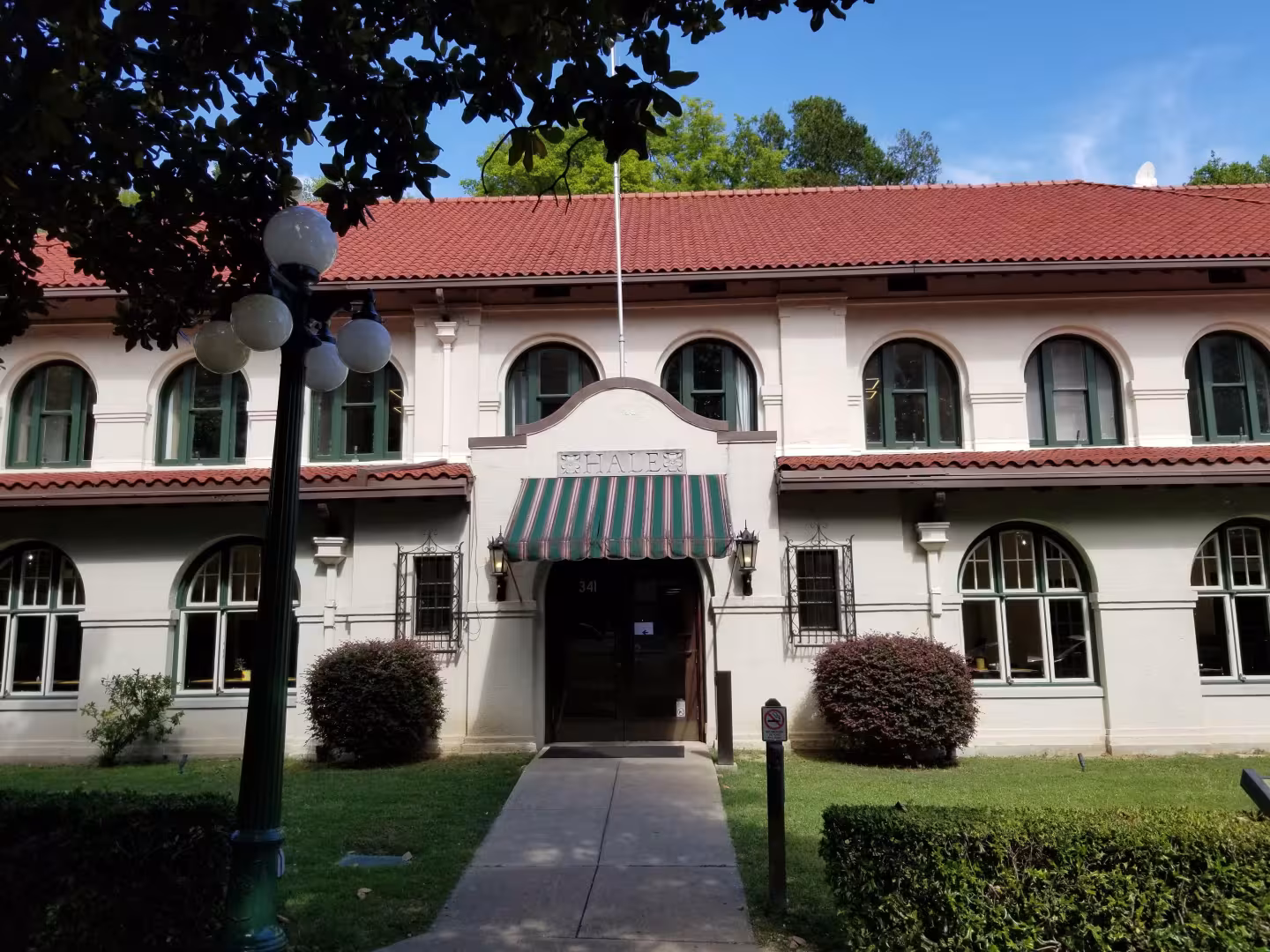 Two-story building with red roof, arched windows, and a striped awning.