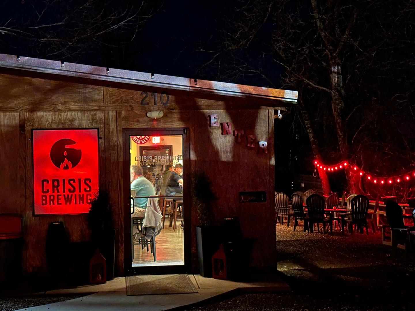 Café entrance at night, red lights and sign, outdoor seating area visible.