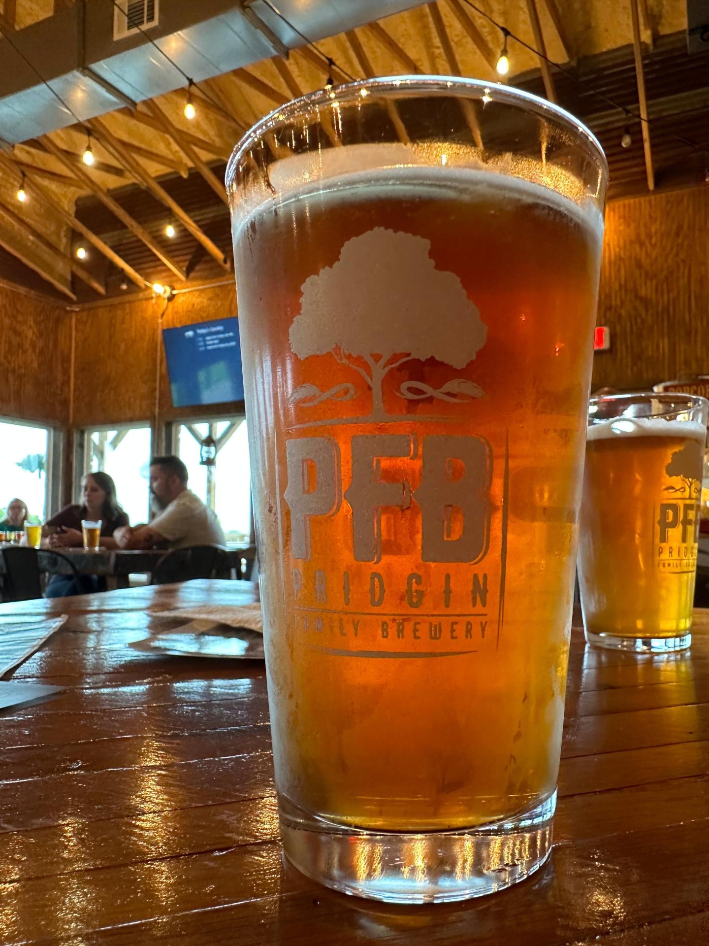 A pint of amber beer on a wooden table in a rustic bar setting.