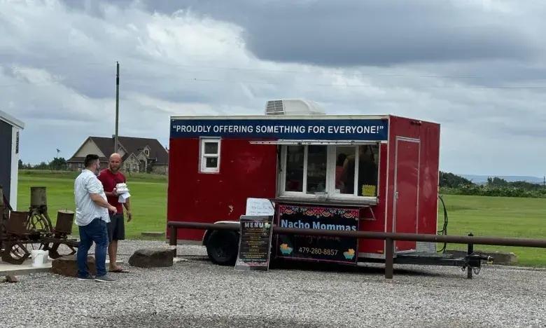 Red food truck with two people standing nearby, cloudy sky in the background.
