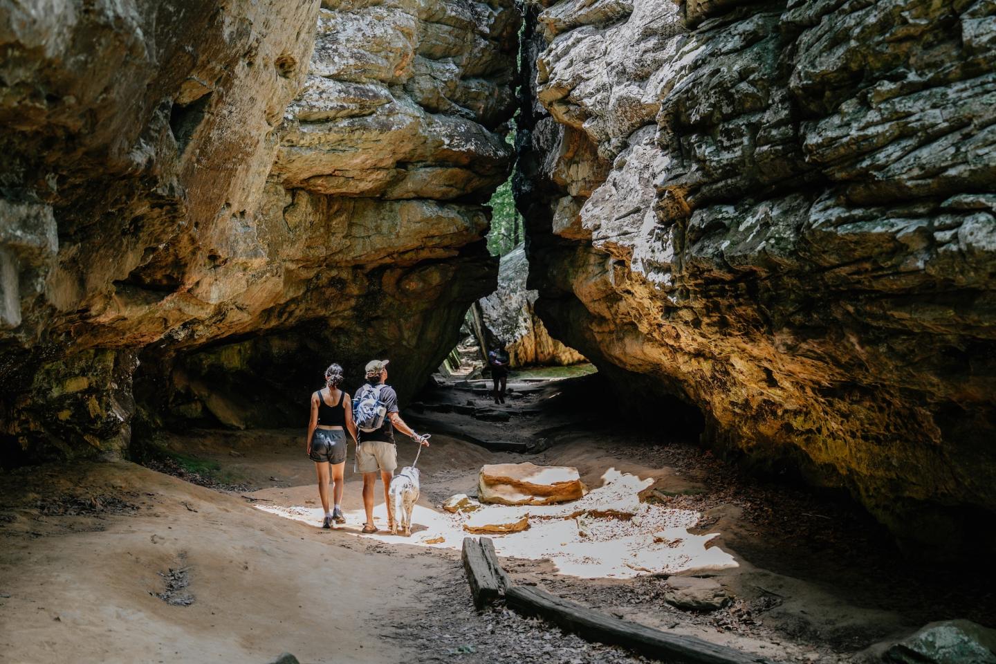 Two people explore a sunlit rocky cave interior.