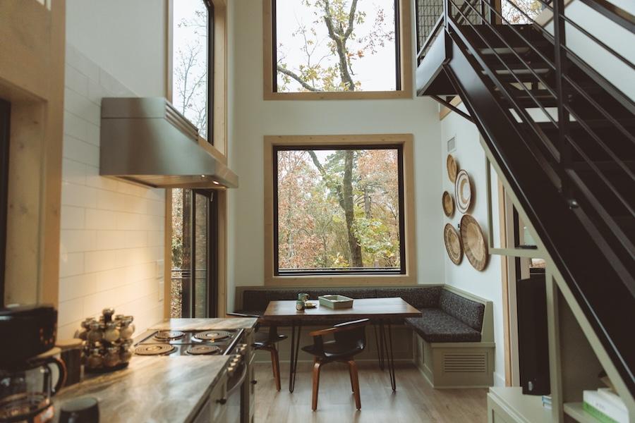 Modern kitchen with large windows and staircase. Cozy dining nook with autumn view.