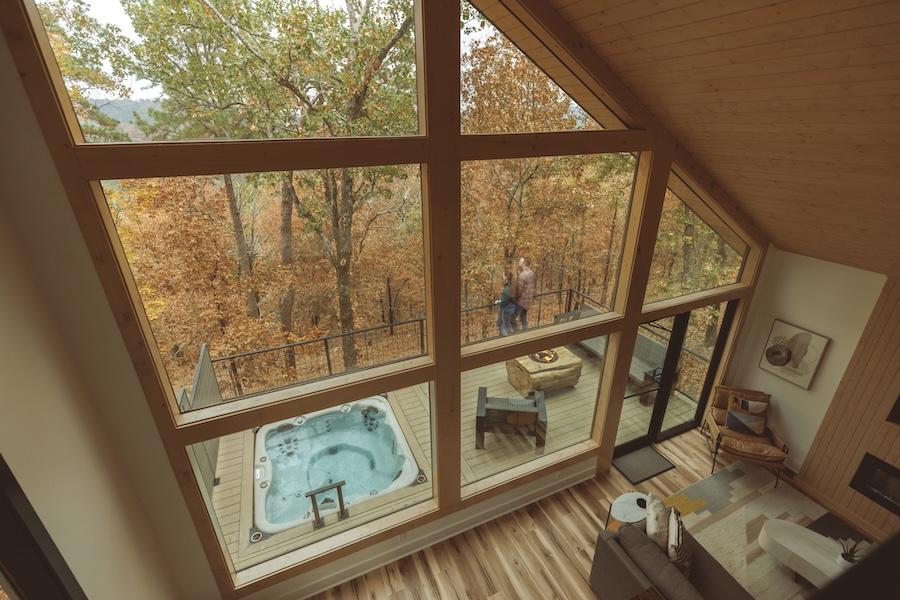 A-frame cabin interior, view of deck with hot tub, surrounded by autumn trees.