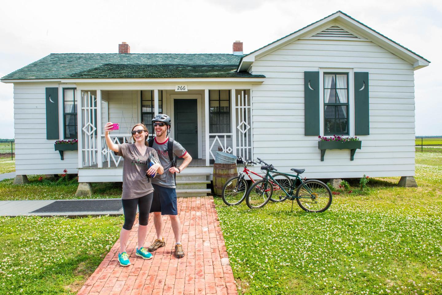 Couple posing happily in front of a white cottage with bicycles nearby.