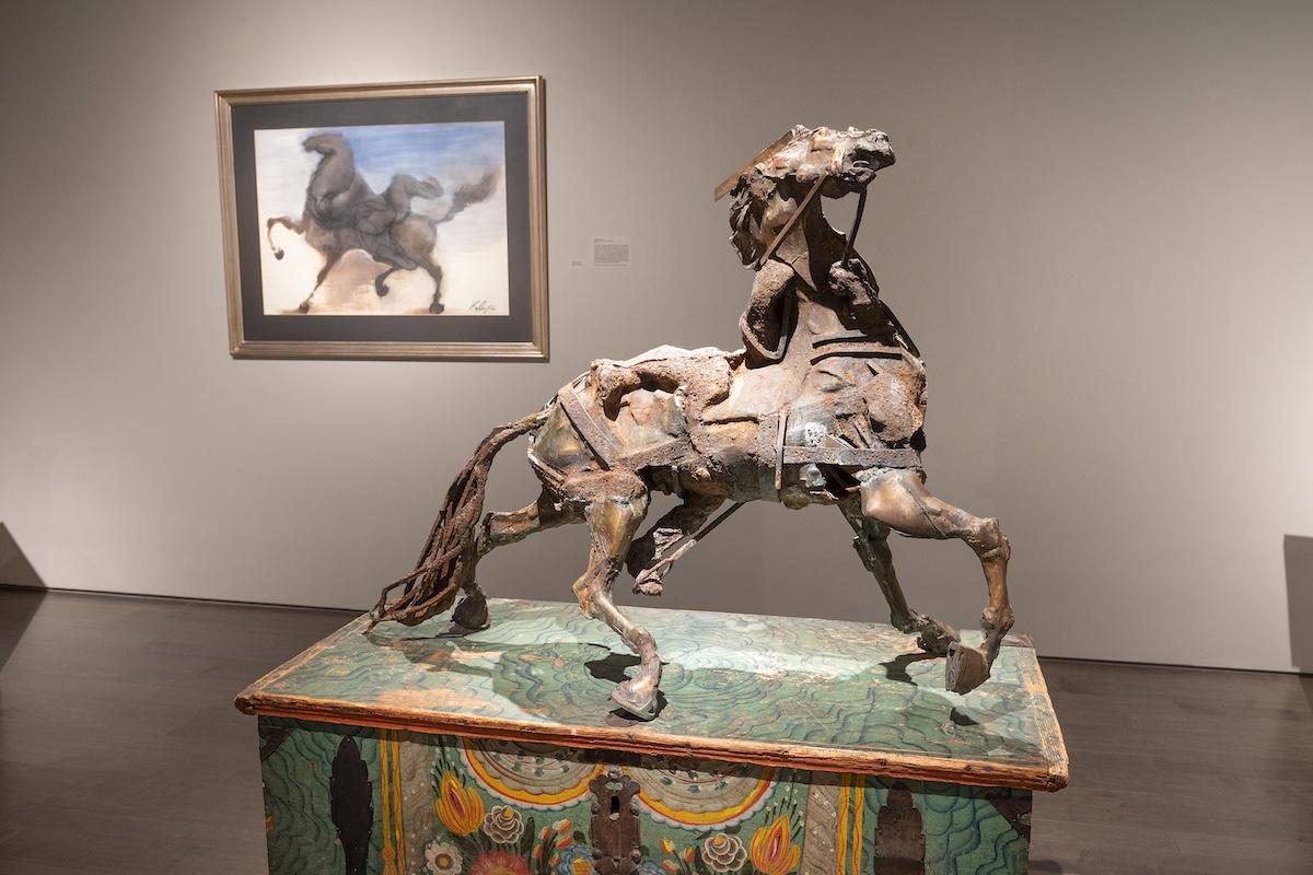 Bronze horse sculpture in a gallery with a horse painting in the background.