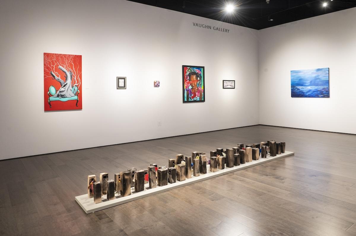 Art gallery with colorful paintings on walls, wooden floor, and a row of sculptures.