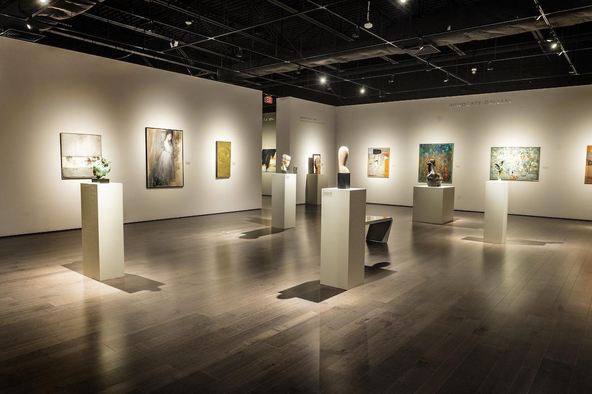 Art gallery with paintings and sculptures on display under soft lighting.