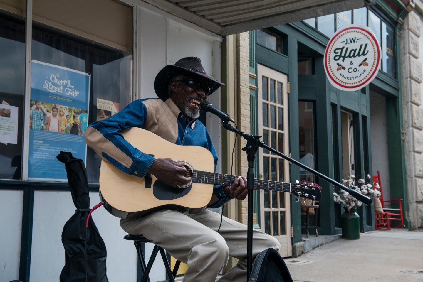 Musician playing guitar and singing on a city sidewalk.