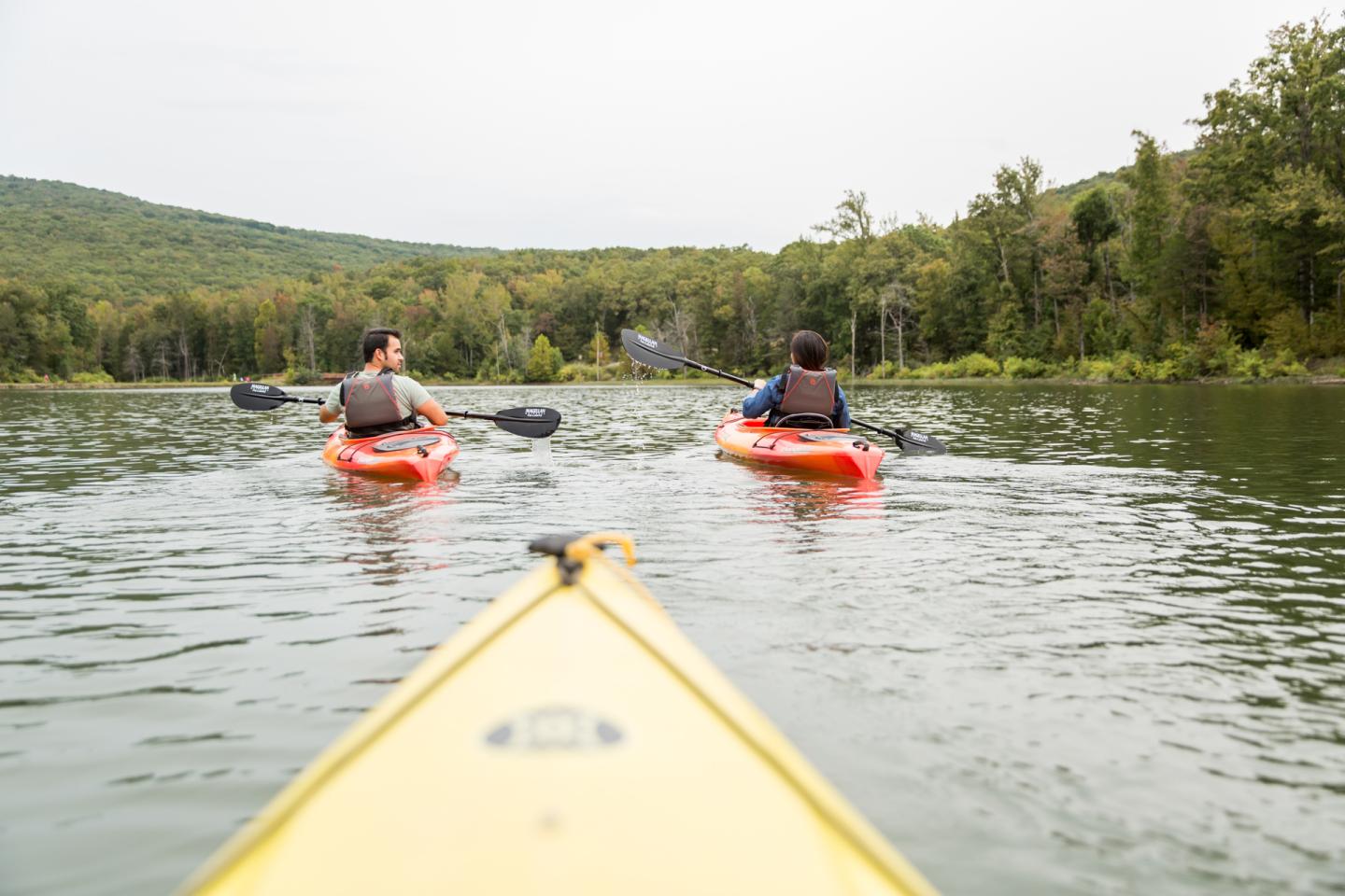 Three people kayaking on a calm lake surrounded by trees.