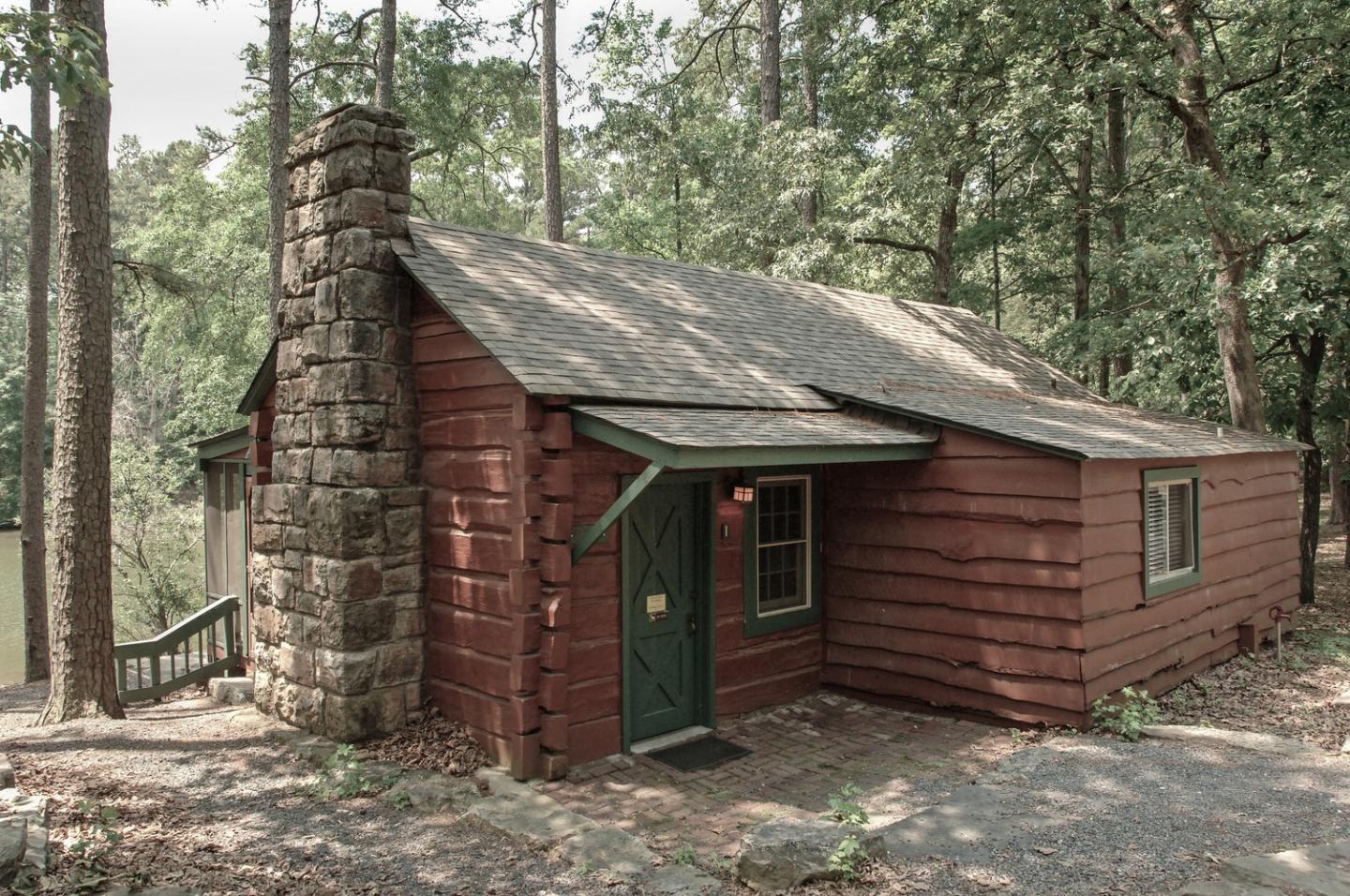 Small wooden cabin with stone chimney surrounded by trees.