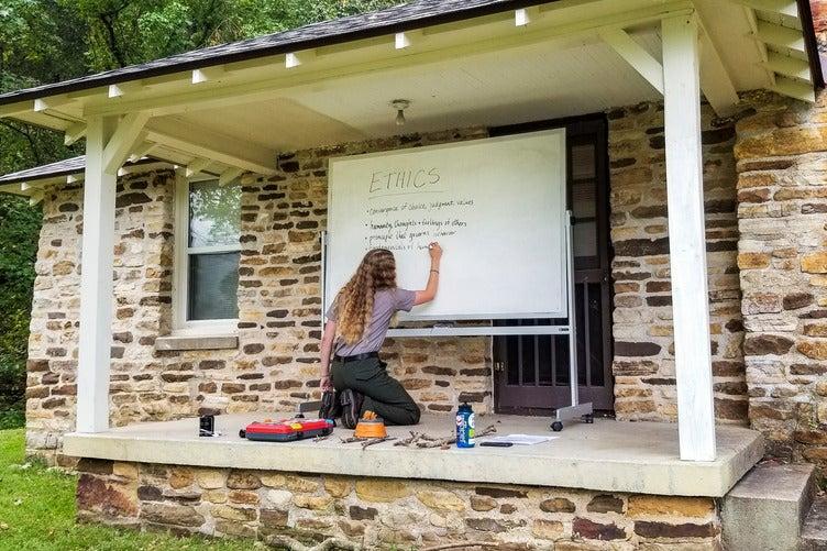 Person writing on a whiteboard outside a stone building.