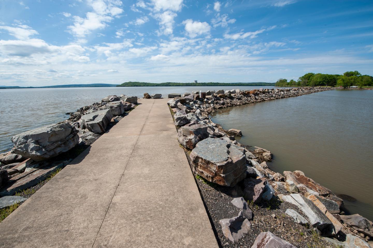 Stone pathway between bodies of water under a blue sky with clouds.