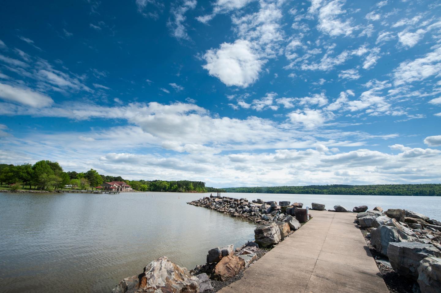 Pathway along a rocky shoreline under a bright blue sky with clouds.