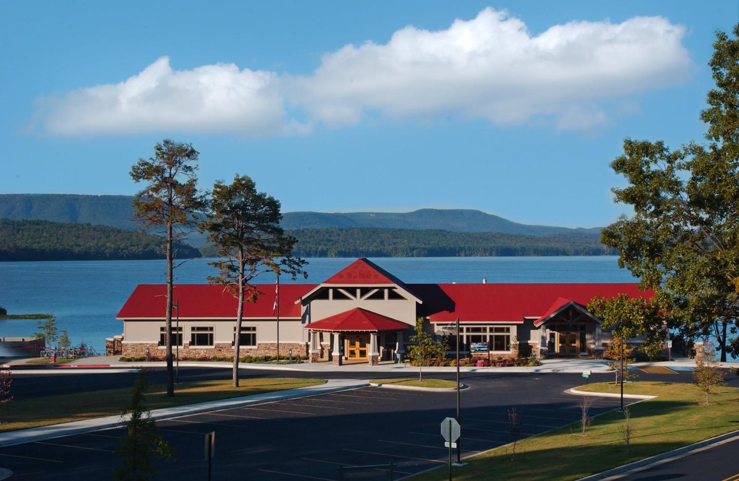 Lakeside building with a red roof, parking lot, and mountains in the background.