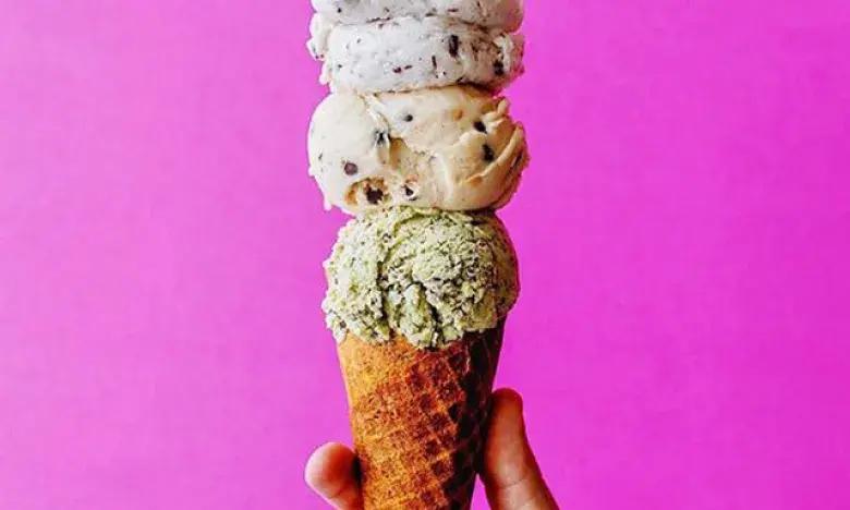 Triple-scoop ice cream cone held against a bright pink background.