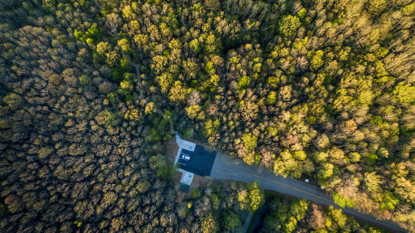 Aerial view of a small parking lot nestled in a dense forest with a winding road.
