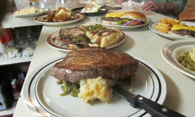 Steak on mashed potatoes and beans, surrounded by various plated meals.