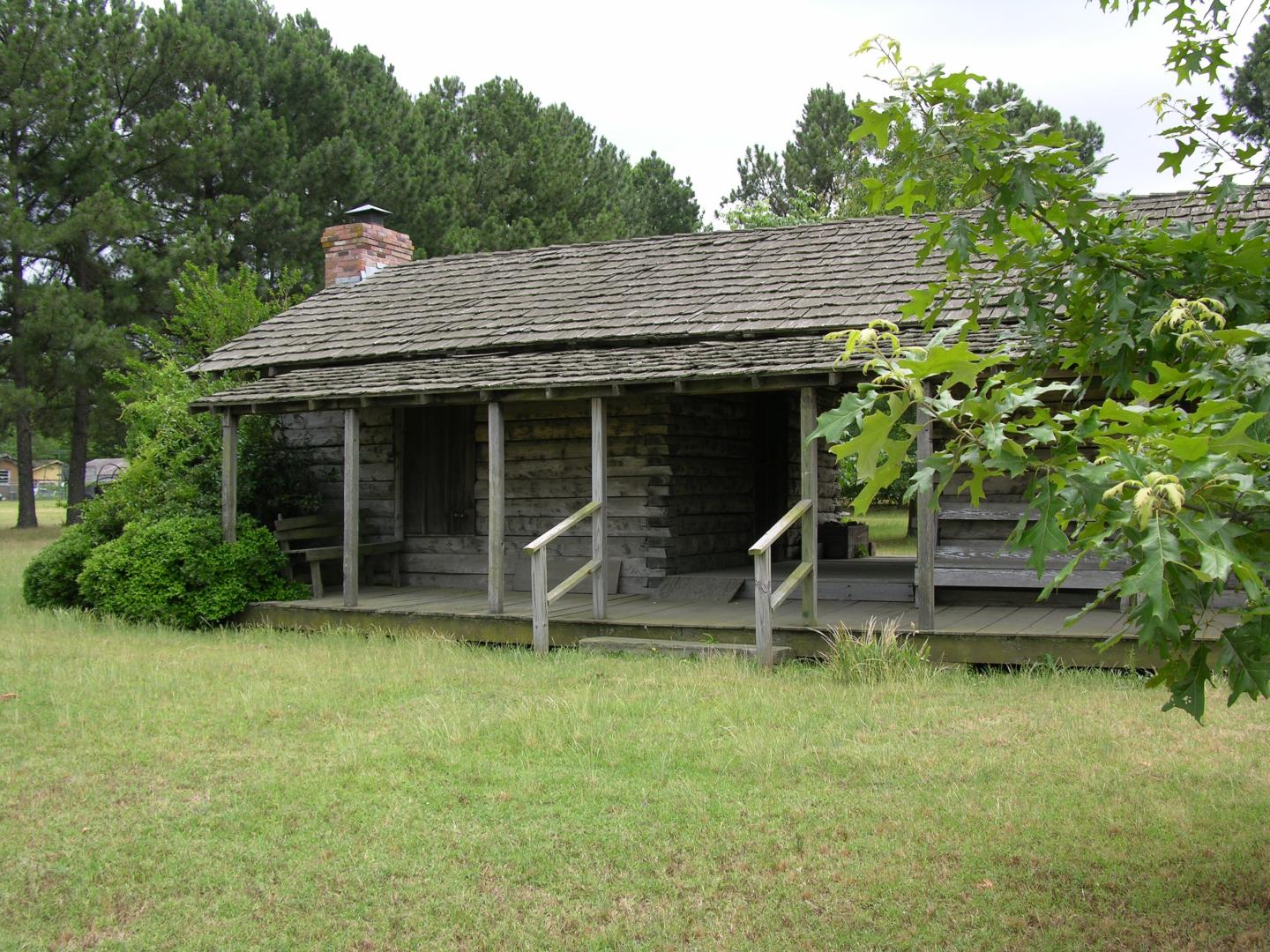 Rustic log cabin with a porch surrounded by trees.