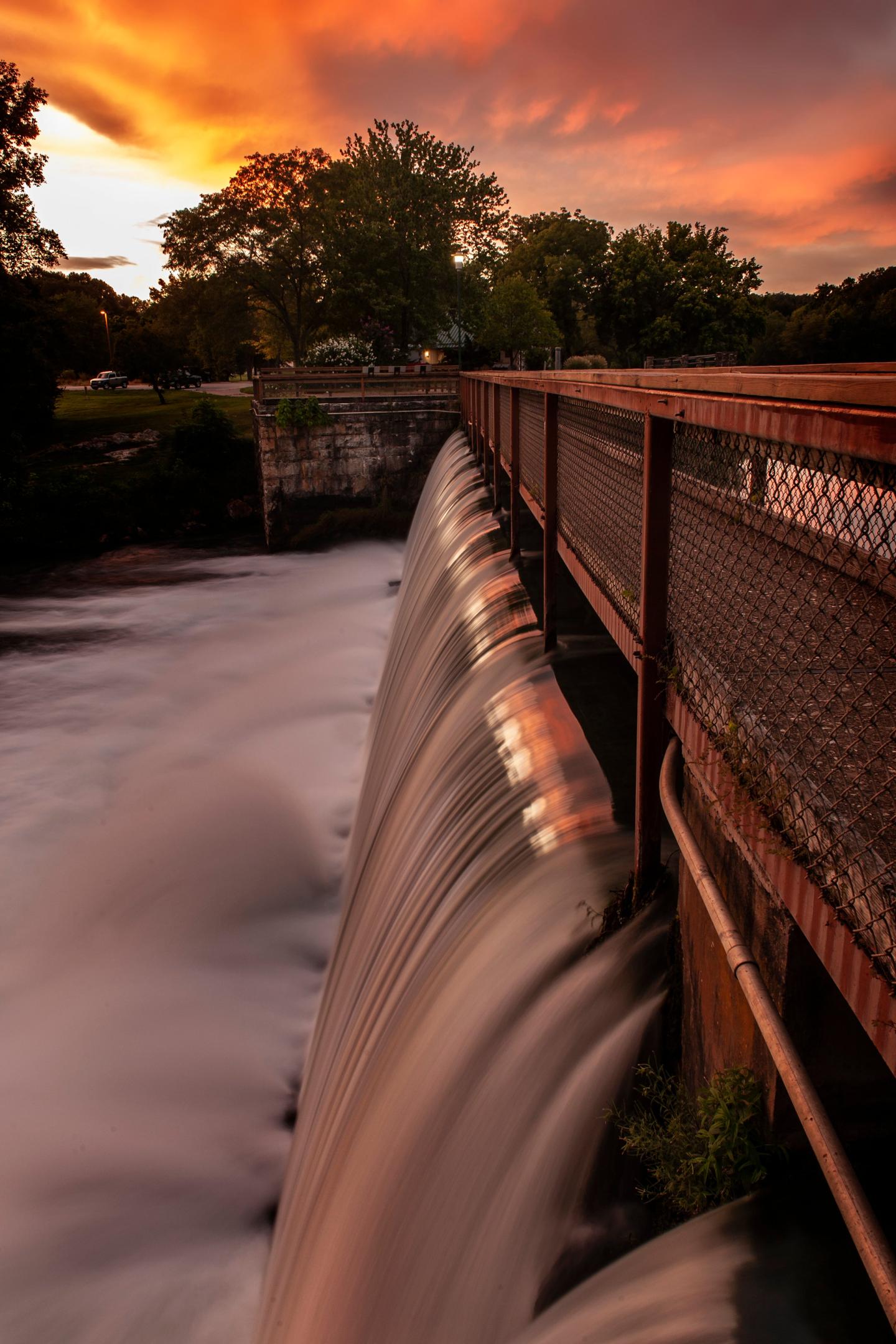 Waterfall at sunset with a vibrant sky and trees in the background.