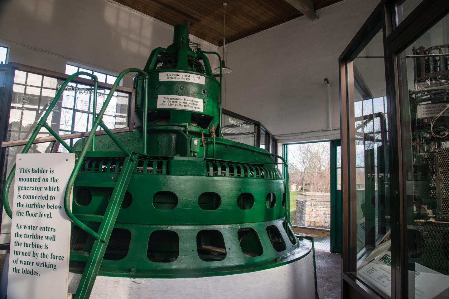 Large green industrial machine inside a building with glass windows.