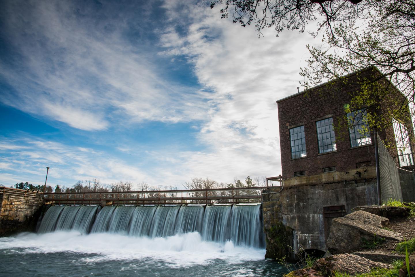 Dam waterfall beside a brick building, under a partly cloudy sky.