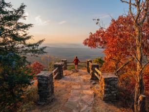 Person overlooks scenic autumn vista with vibrant red and orange foliage.