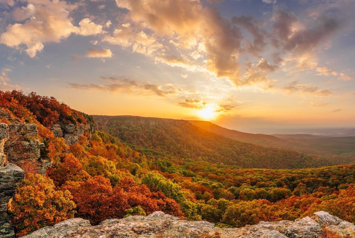Sunset over a vibrant autumn landscape, with colorful foliage and rocky cliffs.