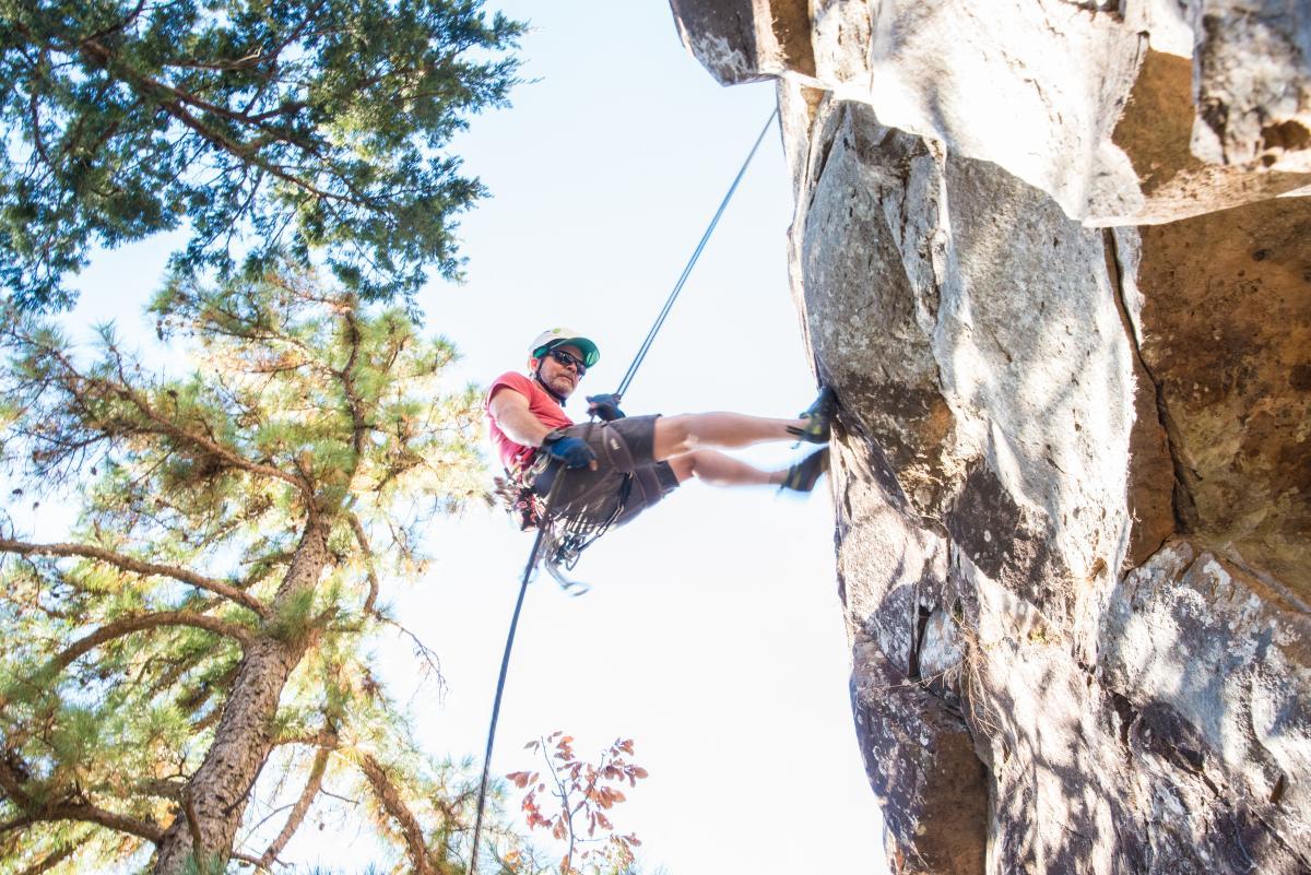 Rock climber rappelling down a cliff, surrounded by trees.