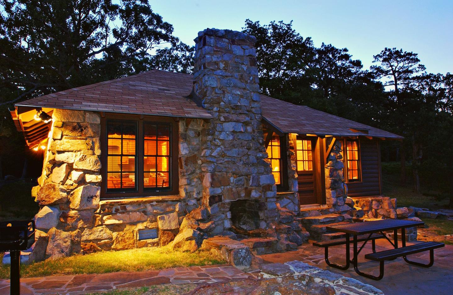 Rustic stone cabin with glowing windows at dusk.