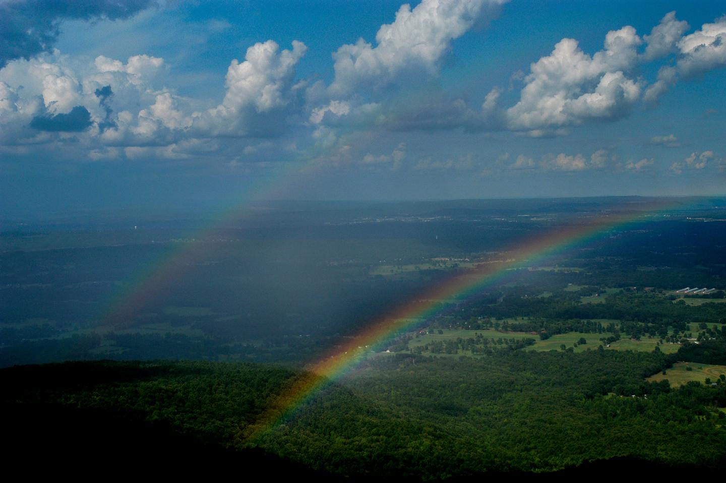 Two rainbows over a lush green landscape beneath a partly cloudy blue sky.