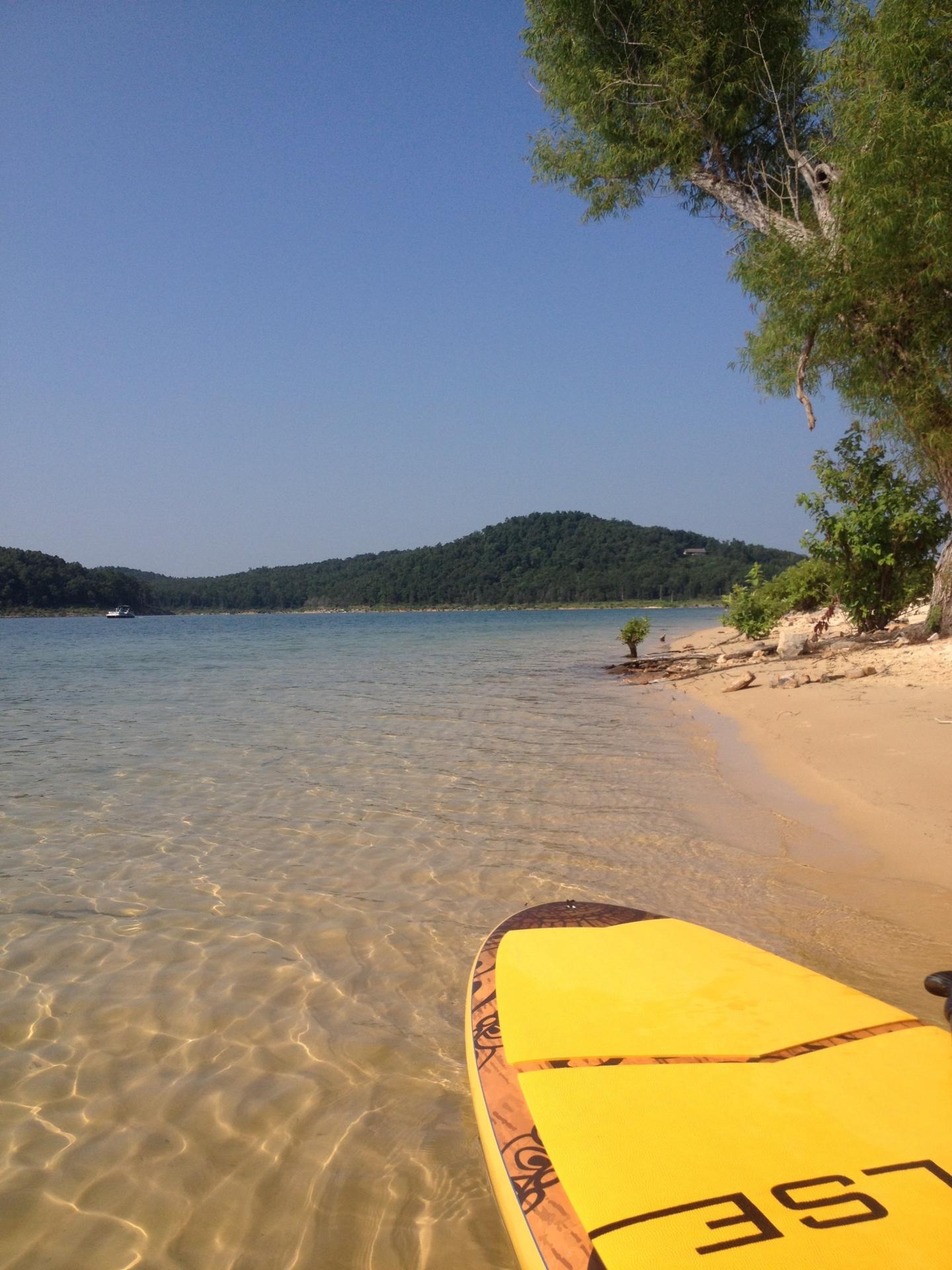 Yellow paddleboard on a clear lake with distant forested hills.