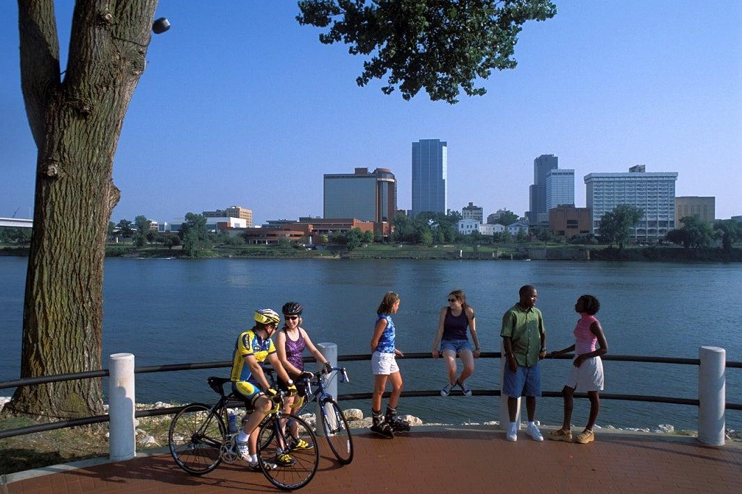 Cyclists and friends enjoy the riverside with city skyline in the background.