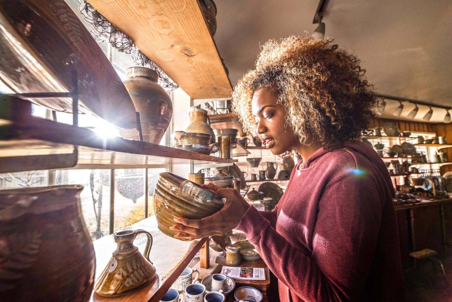 Woman examining pottery in a sunlit shop.