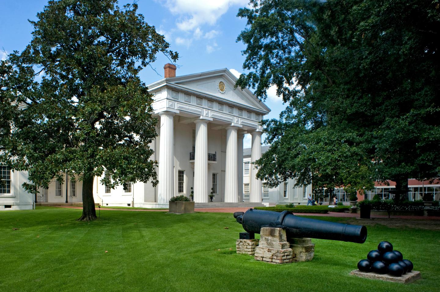 Historic building with columns, grassy lawn, and a cannon in the foreground.