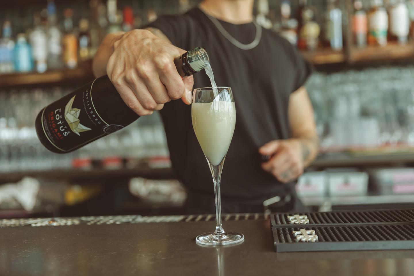 Bartender pouring champagne into a flute glass at a bar.