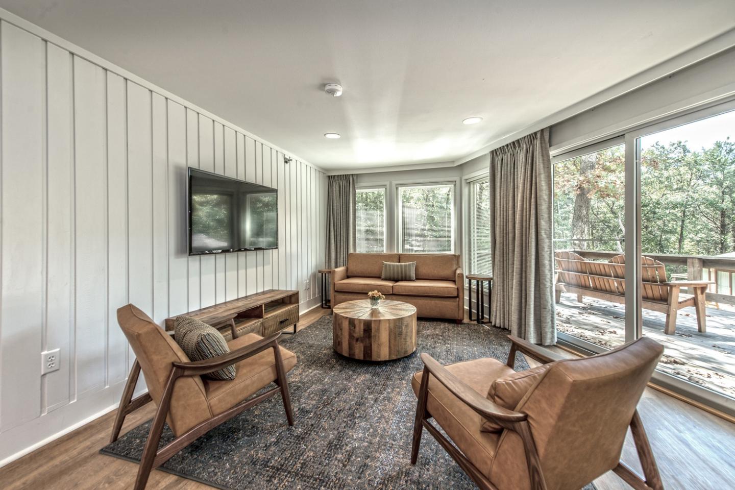 Cozy living room with brown seating, TV, and a large window view of trees.