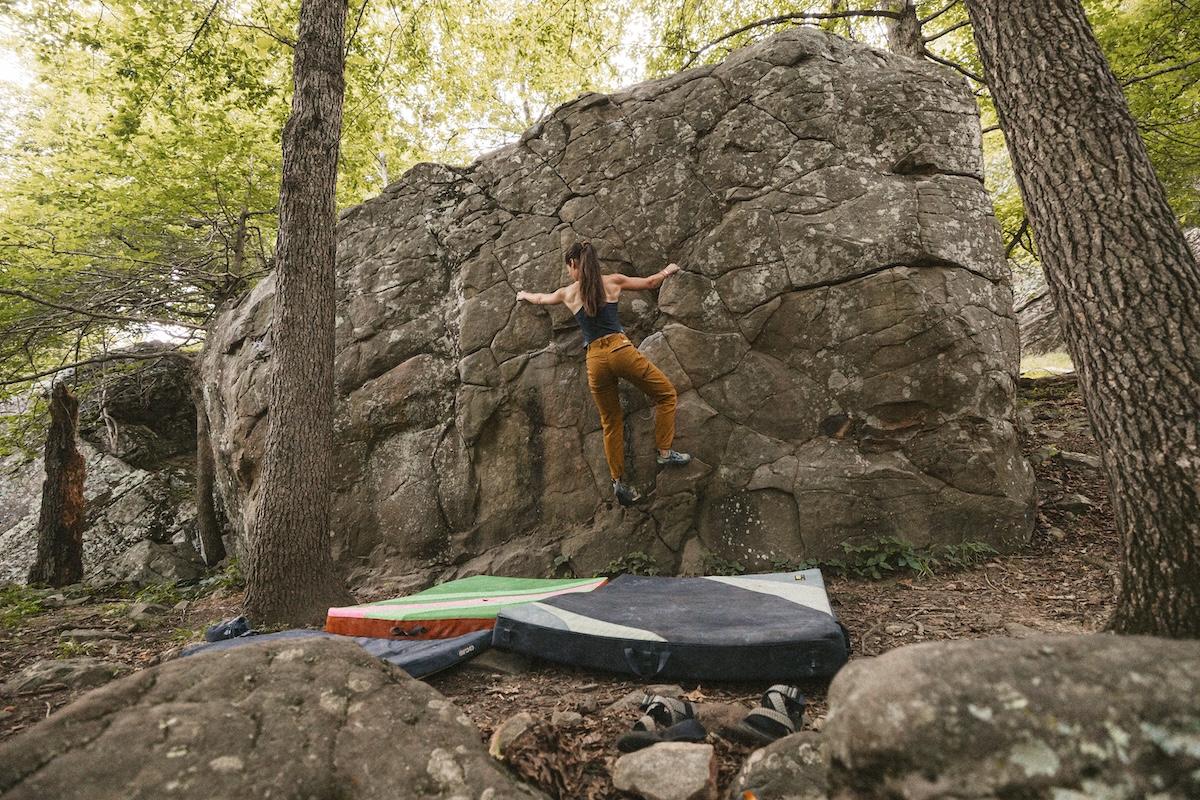 Rock climber ascending a boulder in the forest, with crash pads below.