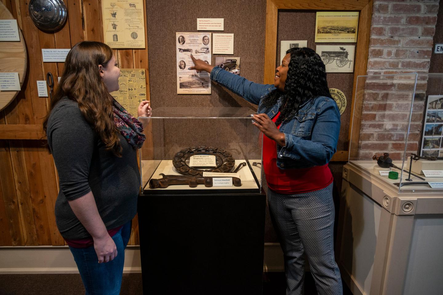 Two women discussing exhibits in a museum, one pointing at a wall display.