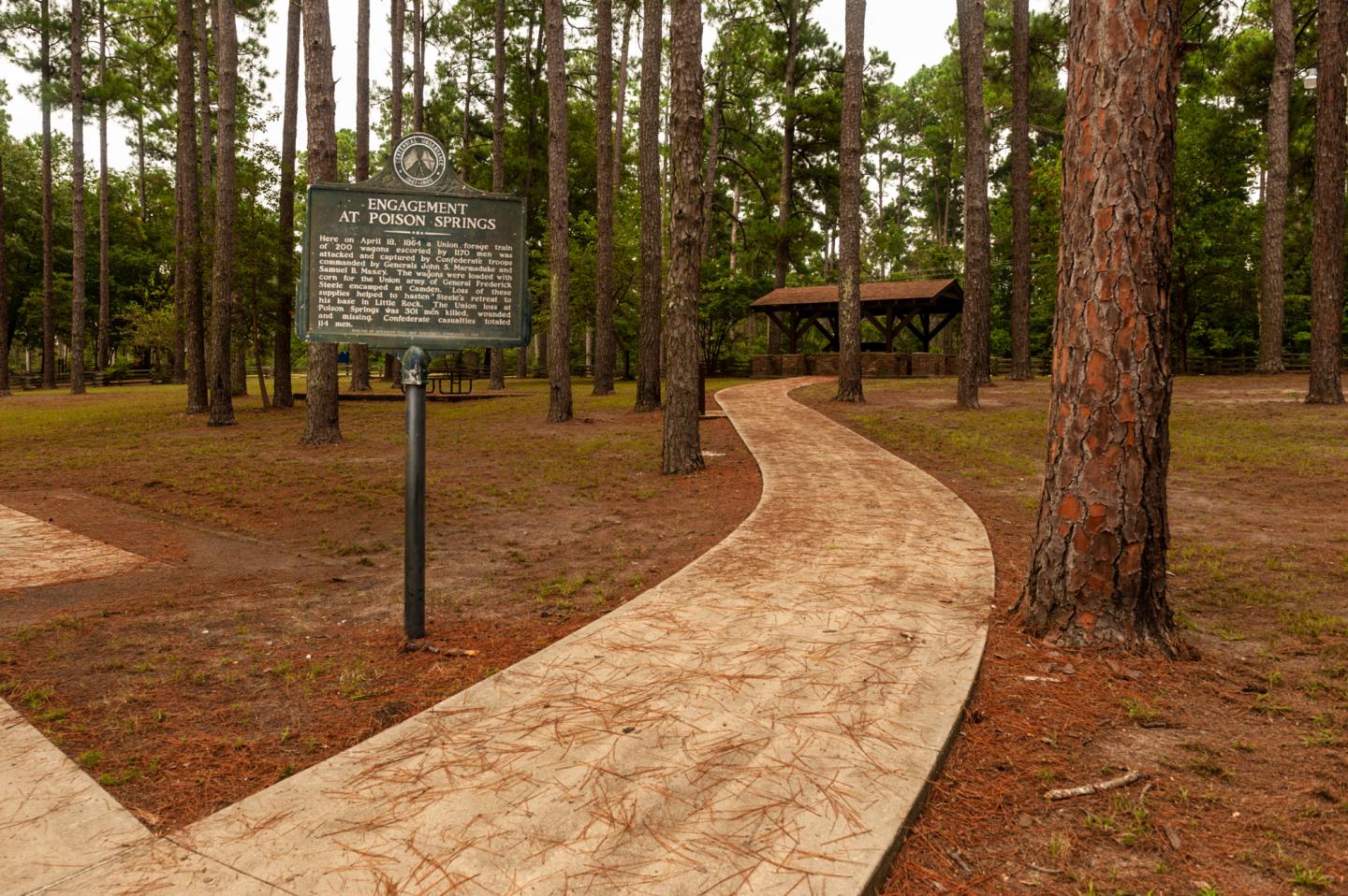 Curved path through a forest with a wooden sign and pavilion.