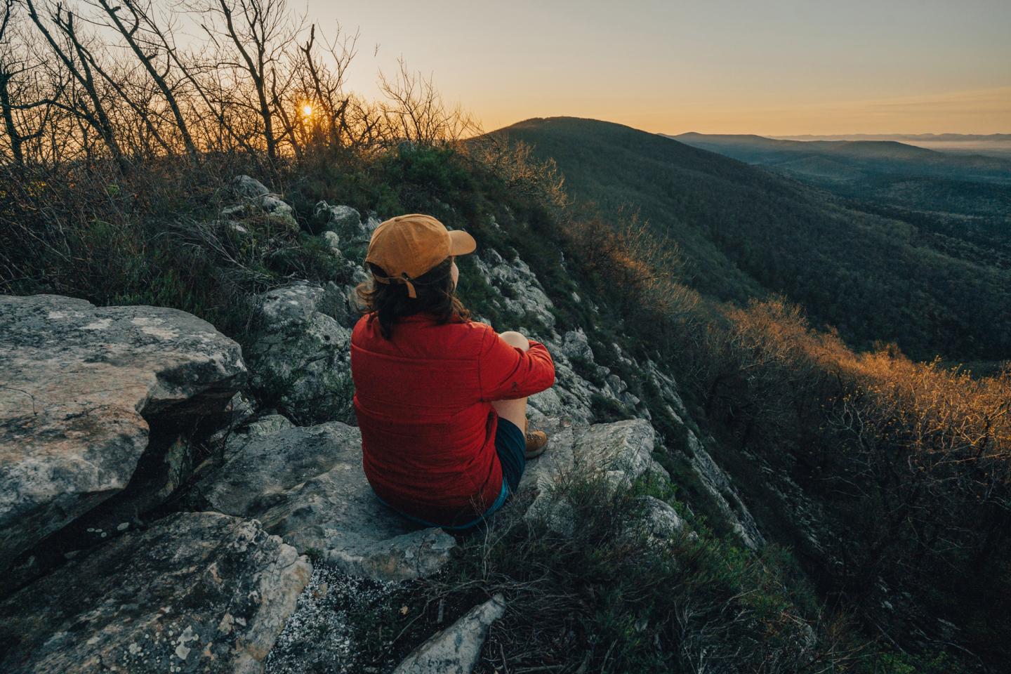 Person in red jacket watching sunset on a rocky hilltop.