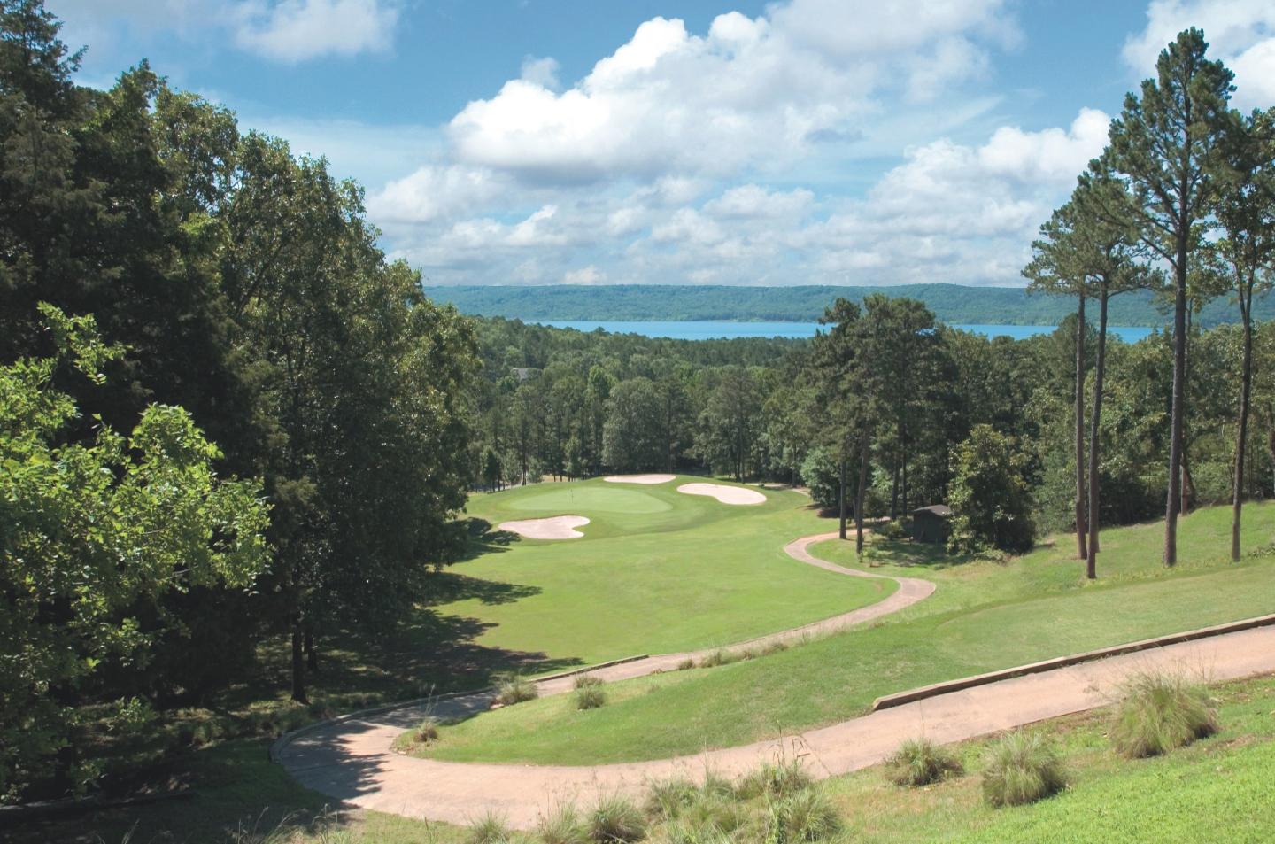 Golf course with trees, blue sky, and a lake in the background.