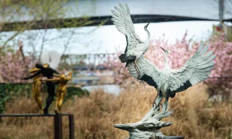 Two bird sculptures amid blooming trees and tall grass.