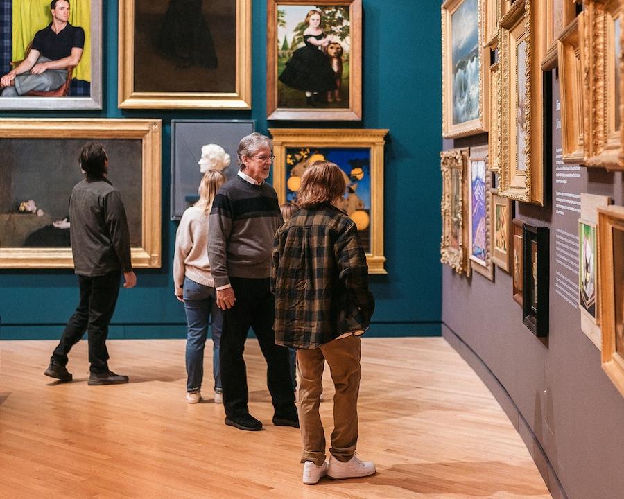 Museum visitors admire framed art on gallery walls.