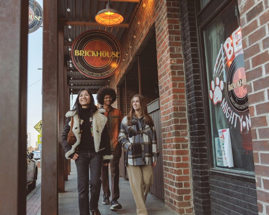 Three people walking on a brick sidewalk under a restaurant sign.