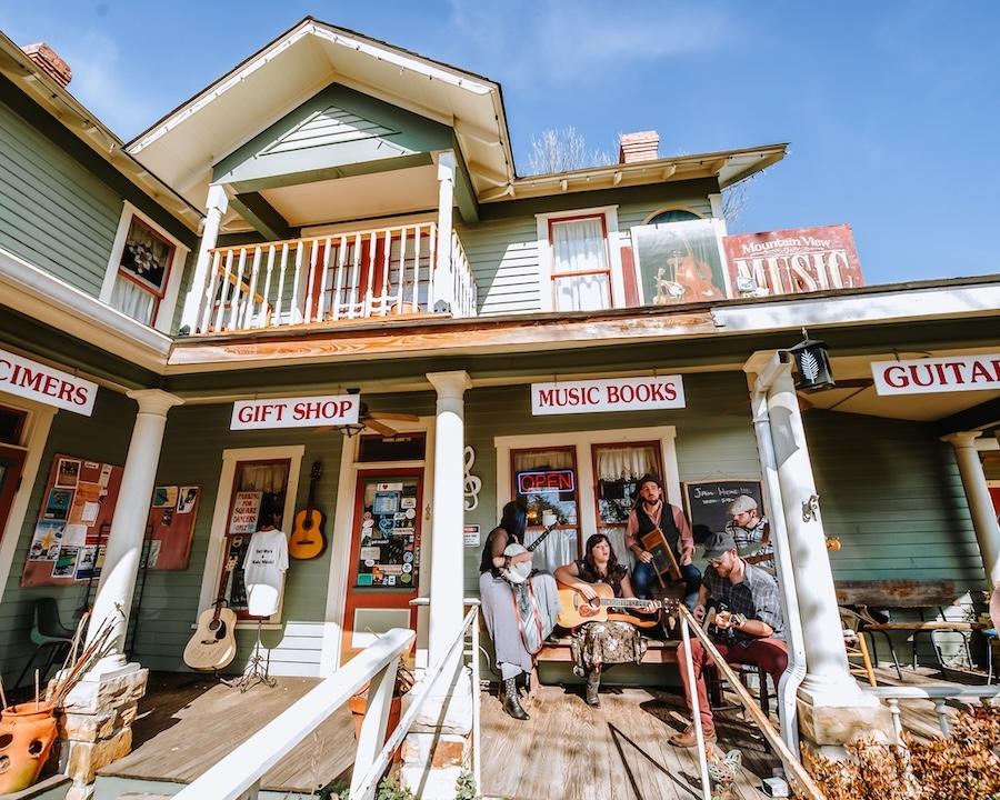Two-story shop with people sitting on the porch, sunny day.