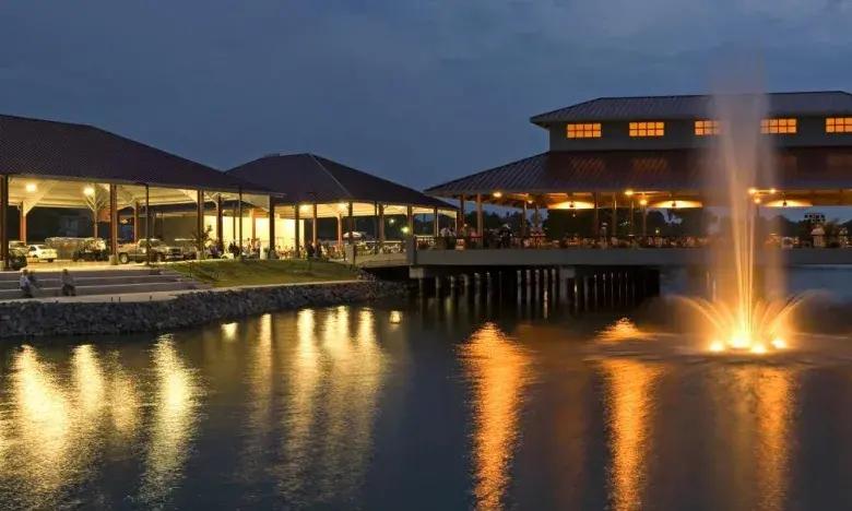 Lit buildings reflected on a pond at dusk with a fountain.