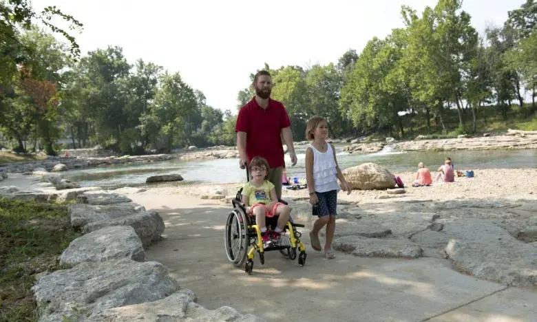Father with two children, one in a wheelchair, enjoying a riverside park.